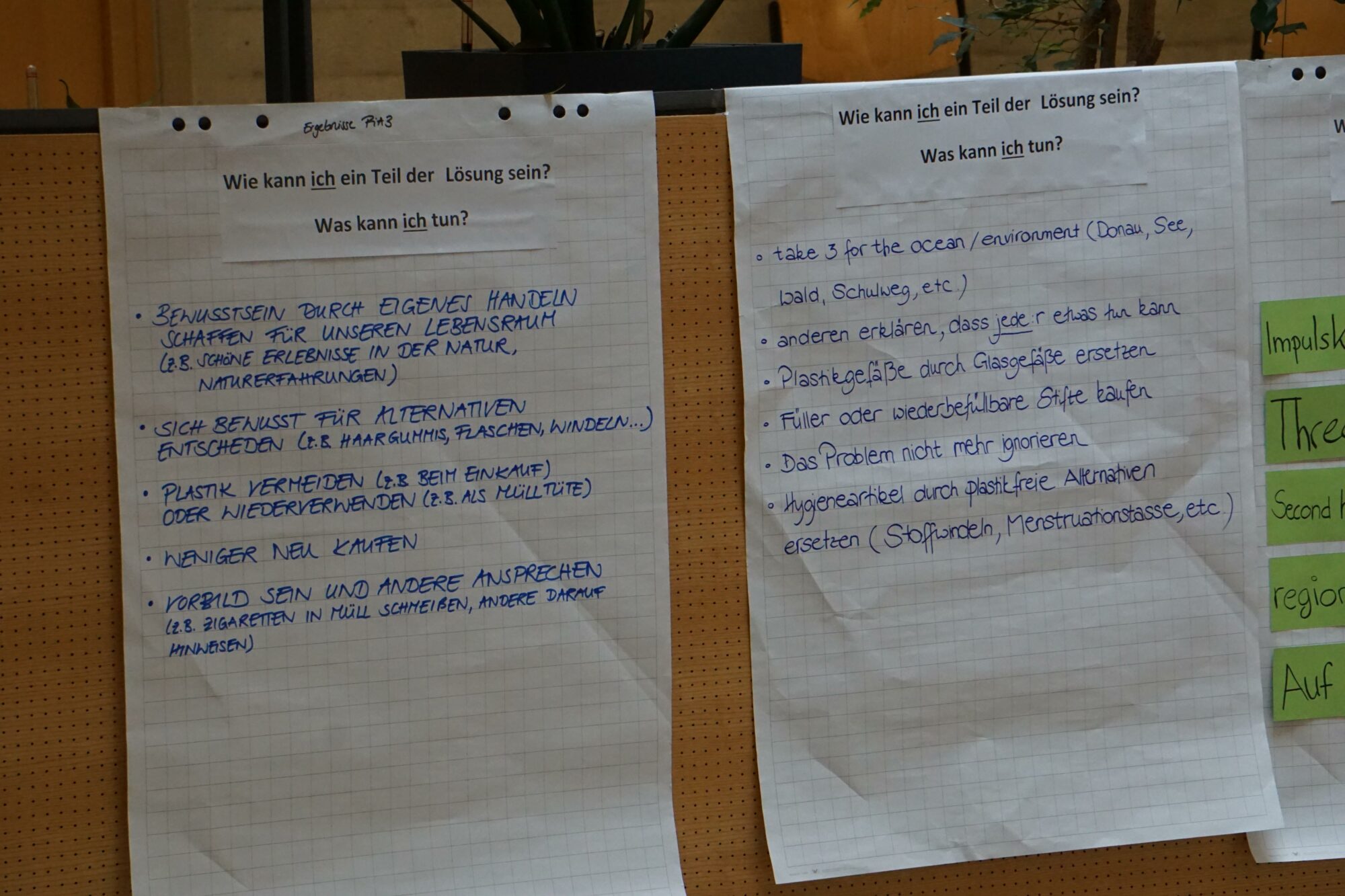 An einer Tafel sind zwei große Blätter mit handschriftlichen Notizen in deutscher Sprache befestigt, auf denen Möglichkeiten zur Mitwirkung an einer Lösung erörtert werden. Die Listen enthalten Aktionen und Ideen, die mit blauem Marker unter den Überschriften geschrieben sind.